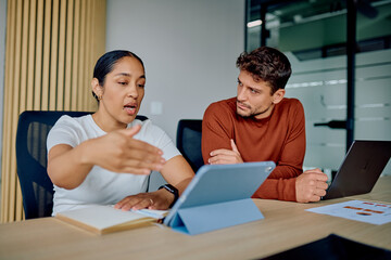 Diverse business colleagues discussing ideas and strategy, working with a tablet and laptop in a modern corporate office