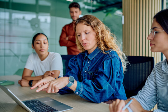 Diverse business professionals working together, discussing ideas and pointing at a laptop screen in a modern corporate meeting room