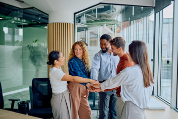 Diverse business professionals joining hands, symbolizing collaboration, teamwork, and success in a modern office environment © we.bond.creations