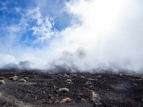 View of volcanic ground contrasting with the bright sky and heavy clouds rolling over the landscape, El Teide National Park, Tenerife, Spain.