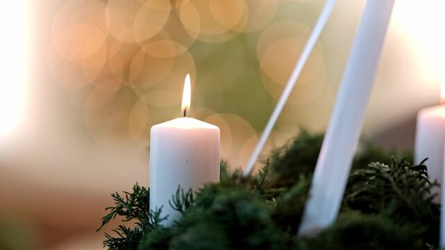 A white Christmas advent candle burning on a wreath with a Christmas tree in the background