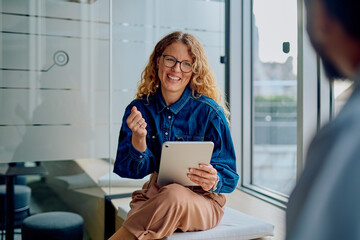 Smiling businesswoman sitting in a modern office, engaged in a conversation while holding a digital tablet