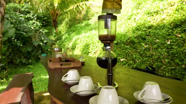 Brewing fresh coffee using siphon extractor on table in lush outdoor setting