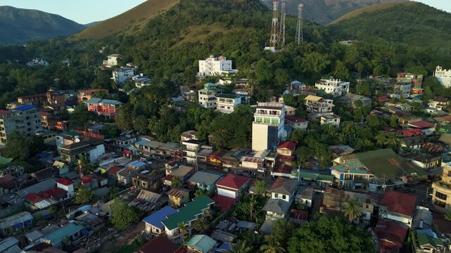 Aerial hyperlapse over Coron Town buildings and hillside cell towers with green mountains and warm golden hour light on Busuanga Island