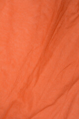 A vertical close-up shot of a textured, wrinkled, orange-brown or terracotta colored woven fabric