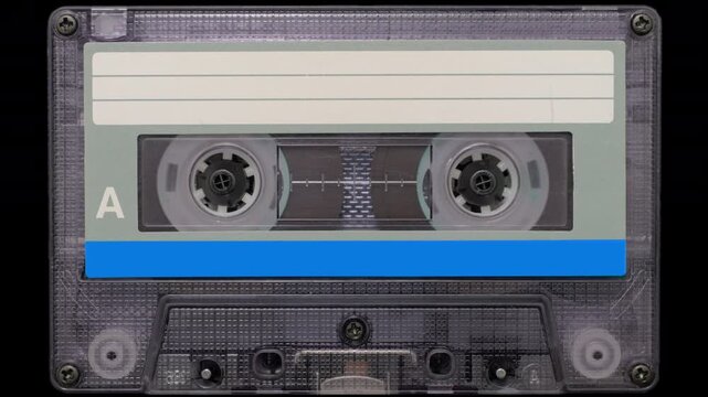 Vintage Audio Cassette Reels Spinning. Retro compact cassette tape with spinning reels on black background.	