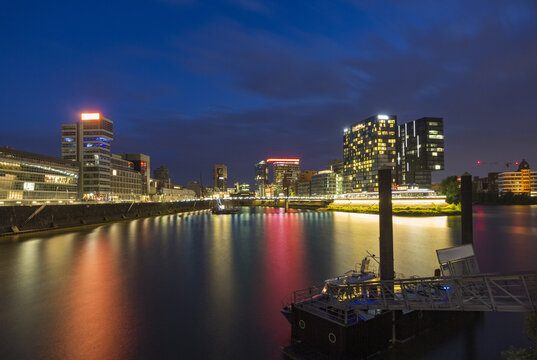 Fototapeta View of the glowing city lights reflecting in the tranquil water, a boat gently bobbing, creating a serene urban nightscape, Dusseldorf, Dusseldorf, Germany.