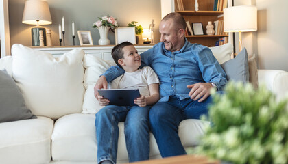 Tablet, relax and father with child on sofa playing online video game in living room at home. Happy, bonding and dad teaching boy kid esports on digital technology for fun together in lounge at house