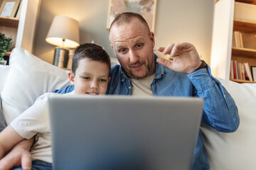 Home, dad and boy with laptop for video call on sofa in living room for communication and networking. People, parent and kid with smile or happy on couch in lounge with wave, fun and bonding,