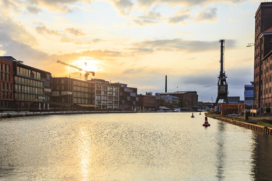 View of the tranquil canal reflecting the golden sunset, buildings, and cranes, a vibrant cityscape at dusk, Stadthafen, Muenster, Germany.