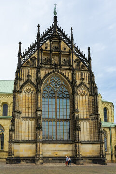 View of the towering, intricately detailed facade of the Dom zu Munster, showcasing its Gothic architecture against a soft, overcast sky, Muenster, North Rhine-Westphalia, Germany.