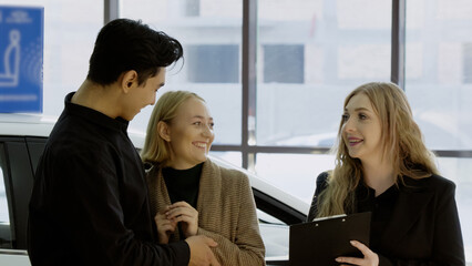 Car dealer explaining features to a couple next to a white modern car