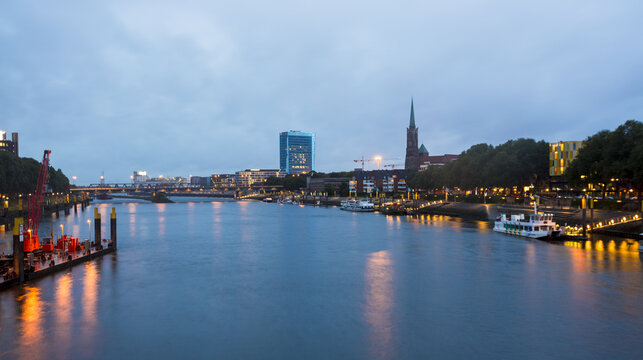 View of the Weser River reflecting the city's lights, bridges, and skyline under a dusky sky, a serene urban scene, Bremen, Bremen, Germany.