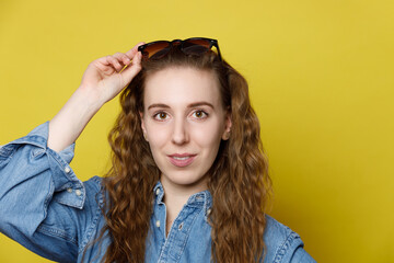 Young Woman Adjusting Sunglasses Against Yellow Background