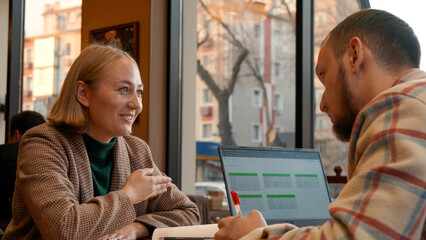 Two young people working together on a laptop in a cozy cafe setting