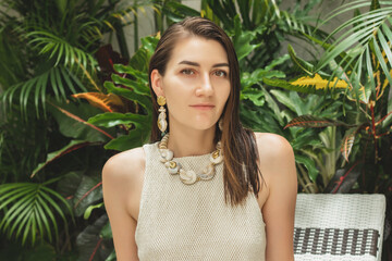 The beautiful woman on the green plants background close up with seashell jewellery set on a Bali villas
