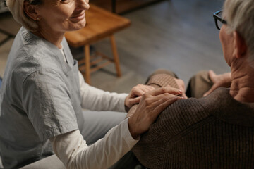 Obraz premium Middle aged Caucasian woman comforting senior Caucasian man by gently placing hand on his shoulder in nursing home setting, both sitting closely and engaging in supportive interaction