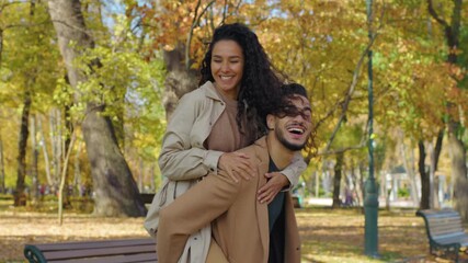 Hispanic happy couple having fun in autumn park man holding woman piggyback spinning whirling around rotating fooling around laughing cheerful outdoors in fall season laughing smiling joy love dating - Powered by Adobe