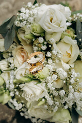 Elegant gold wedding rings on white bridal bouquet with roses