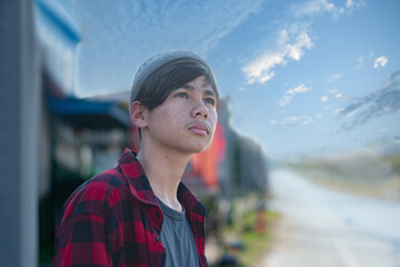 A quiet moment of melancholy. This middle schooler, dressed in a red plaid shirt and a grey knit hat, stands alone with a sad, introverted expression. Capturing the complexity of youthful solitude.
