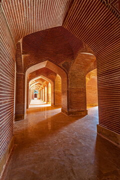 View of red brick arches creating a tunnel-like effect with light and shadow play, showcasing architectural symmetry and depth, Thatta, Sindh, Pakistan.