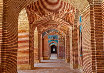 View of intricate brickwork arches and blue tile details create a mesmerizing corridor within a historical building, Thatta, Sindh, Pakistan.