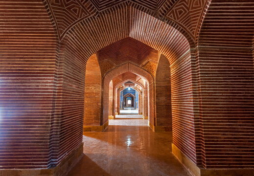 View of intricate brickwork arches create a mesmerizing tunnel, leading the eye towards a distant light in Thatta, Sindh, Pakistan.