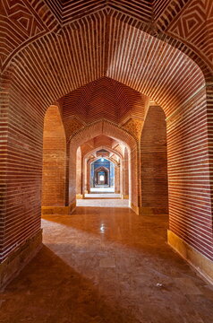 View of warm, textured brick arches receding into the distance, creating a tunnel-like effect with light and shadow playing along the corridor, Thatta, Sindh, Pakistan.