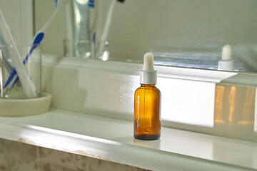 Amber glass dropper bottle on bathroom shelf with reflected light for skincare and aromatherapy.