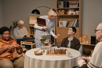 Group of seniors including Black woman knitting, Caucasian man using smartphone, Caucasian woman...