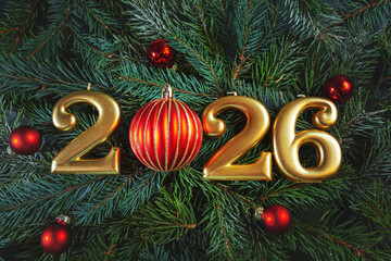Golden numbers 2026 and Christmas balls against a background of fir branches.