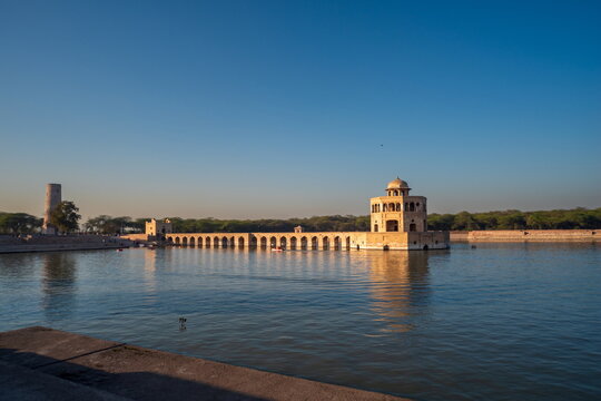 View of the serene Hiran Minar complex reflecting in the tranquil waters under a bright blue sky, a stunning architectural marvel, Hiran Minar, Sheikhupura, Pakistan.