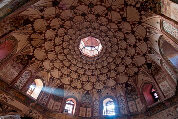 View of a dome ceiling adorned with intricate geometric patterns and a central skylight, casting soft light onto the walls of Shahi Hammam, Lahore, Pakistan.