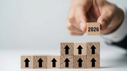 A person building a tower with wooden blocks representing growth and progress towards a goal in 2026 with upward arrows
