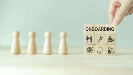 Hand arranging a wood block with the word 'ONBOARDING' on the desk, emphasizing the beginning stages of an employee's professional journey.