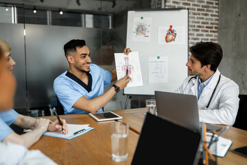 Positive middle-eastern young man chief doctor showing his colleagues presentation, multiethnic team of professional docotrs attending medical conference or having breefing, discussing medical cases