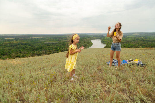 Mother with daughter blowing soap bubbles in field on summer day - Powered by Adobe