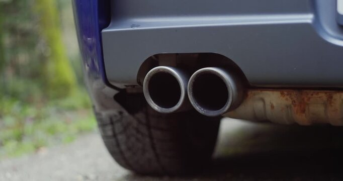 Generic car twin exhaust pipe tips track and pan shot  Low angle, close up shot, blurry nature background, dynamic real time video, no people