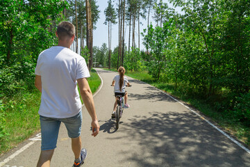 Dad teaches daughter to ride a bike. Girl sat on bicycle for the first time, his father teaches child to ride a bicycle.