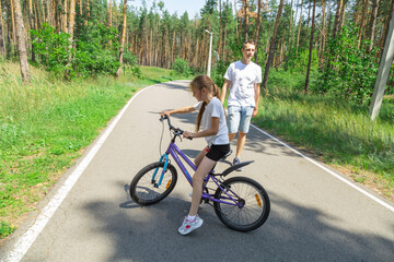 Dad teaches daughter to ride a bike. Girl sat on bicycle for the first time, his father teaches child to ride a bicycle.