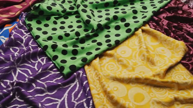 Aerial style slow pan over chaotic layered sheets of abstract fabric displaying bold geometric and flowing organic patterns in high contrast colors aerial, top down view, design