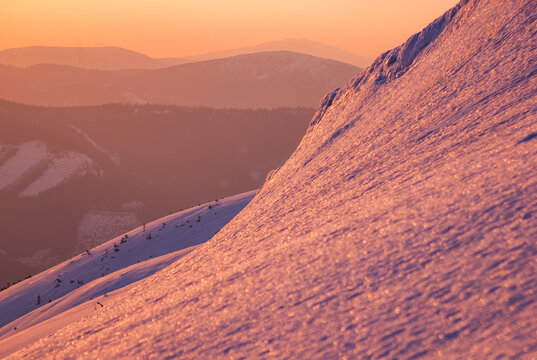 View of a snow-covered mountain slope bathed in the warm glow of the setting sun, with distant peaks fading into the horizon, Rovna hola, Banskobystricky kraj, Slovakia.