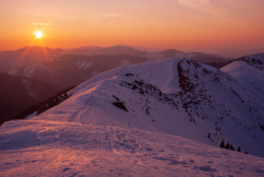 View of the sun setting over the snow-dusted peaks, casting a warm, orange glow on the cold, white landscape, Rovna hola, Banskobystricky kraj, Slovakia.