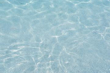 Clear turquoise water, sunlight reflecting, symbolizing natural beauty and serene aquatic scene, bottom through transparent water, blue background, natural resources planet