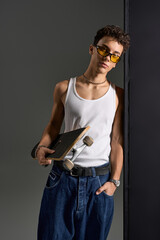 Curly teenager with stylish sunglasses and tank top poses confidently in gray setting