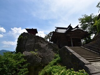 Historic small wooden temple building perched on a massive rock at Risshakuji (Yamadera) temple in Yamagata, Japan, under a blue sky.