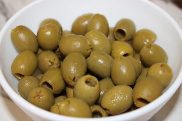 Bowl of green olives served at a kitchen table, ready for a meal or snack during a casual gathering with friends