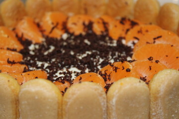 Delicious dessert with layers of cream, mandarin oranges, and chocolate shavings arranged in a round shape on a wooden table