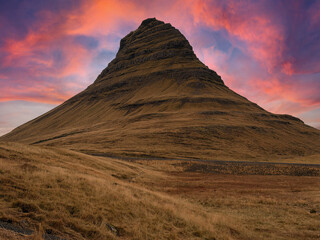 Kirkjufell mountain under a vibrant sunset sky painted in orange, red, and pink hues, creating a dramatic and colorful Icelandic landscape.