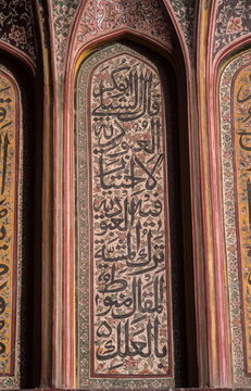 View of intricate Arabic calligraphy adorns a recessed archway, framed by ornate floral patterns in contrasting colors, Lahore, Punjab, Pakistan.